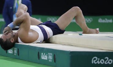 Спортсмен после приземления упал, схватившись одной рукой за травмированную ногу, а правой закрыв лицо.