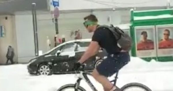 Bărbat surprins în tricou și pantaloni scurți pedalând prin nămeți