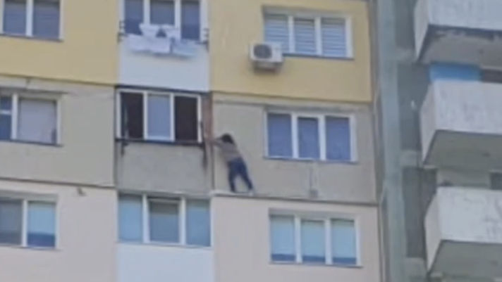 Momentul în care o femeie stă agățată de fereastra unui bloc de locuit