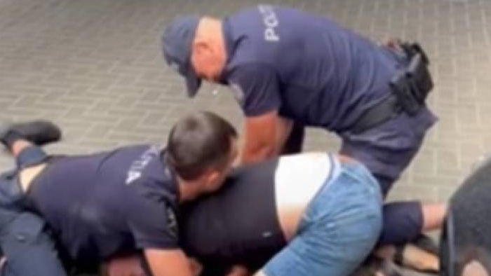Un bărbat, pus cu capul pe asfalt și încătușat de doi polițiști