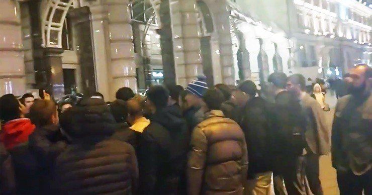 Рядом с отелем находится несколько десятков человек. Недалеко дежурят сотрудники ОМОН, отмечает издание.
