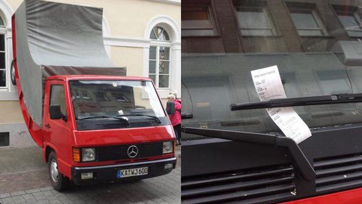 Ярко-красный тентованный фургон Mercedes-Benz "припаркован" передней частью на мостовой.