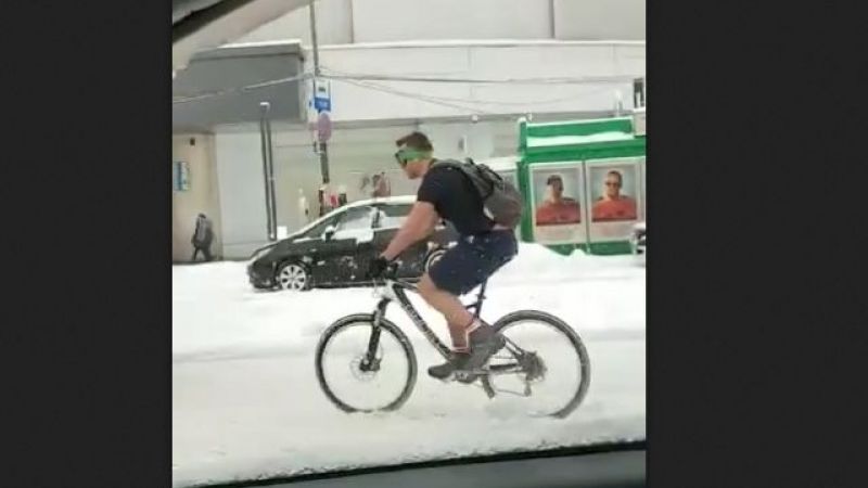 Bărbat surprins în tricou și pantaloni scurți pedalând prin nămeți
