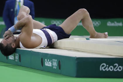Спортсмен после приземления упал, схватившись одной рукой за травмированную ногу, а правой закрыв лицо.