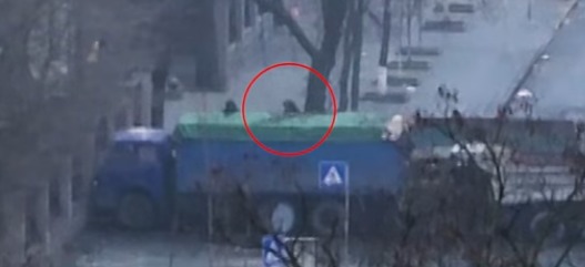 Огонь ведется из-за грузовиков, которые стоят перед бетонными баррикадами, людьми в черной форме.