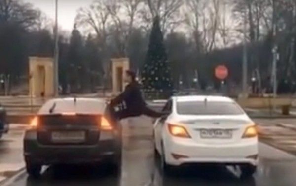 Мужчина сел на шпагат между двумя движущимися машинами. 