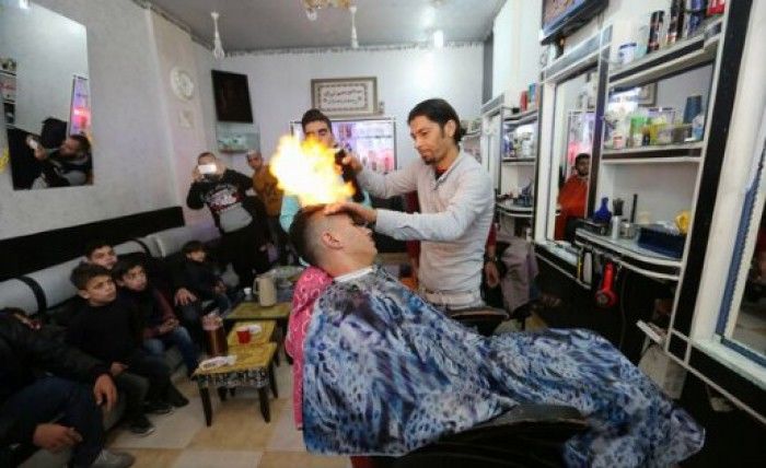 Ramadan Odwan aprinde jetul spray-ului folosind bricheta și trece flacăra prin părul clientului aflat pe scaun. Foto: REUTERS 