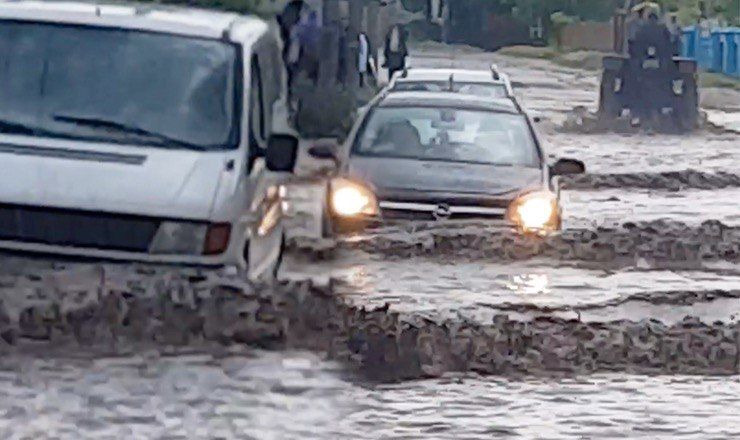 На видео видно, что недавние дожди сильно затопили улицу, по которой автомобили едва могут ехать.