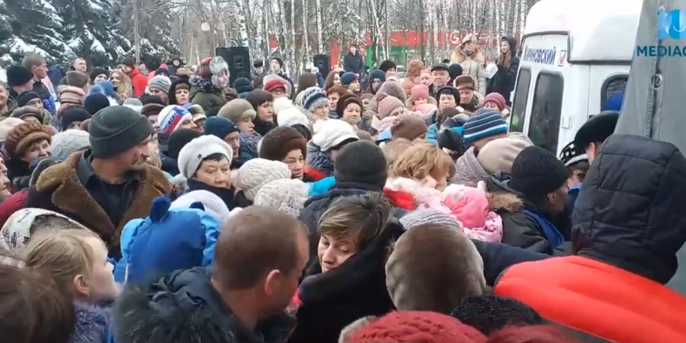 На кадрах запечатлены горожане, толпящиеся вокруг машин, где раздают наборы конфет. 