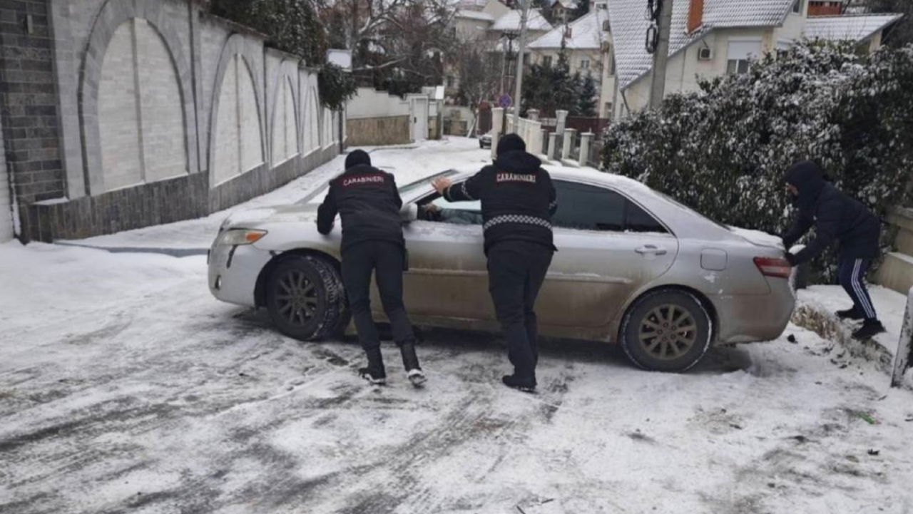 Un șofer blocat pe un carosabil alunecos, ajutat de carabinieri.