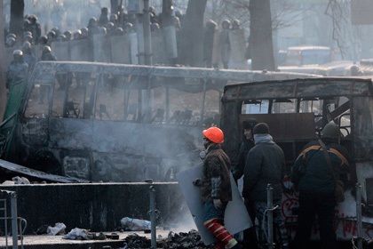 Протестующие прячутся за обгорелыми остовами автобусов милицейского оцепления на улице Гущевского в Киеве. Фото: сергей Чузавков / AP