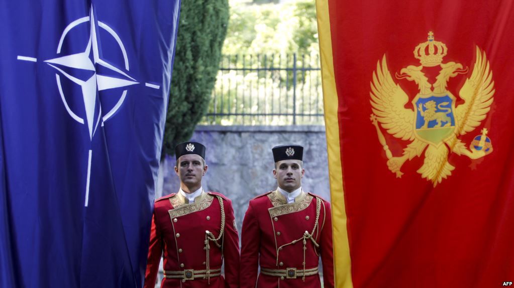 Membri ai gărzii de onoare lîngă drapelele Muntenegrului și NATO la o ceremonie în Podgorița.