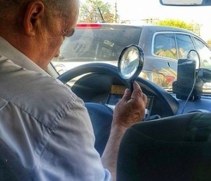 Un taximetrist din capitala isi verifica comenzile pe telefon cu lupa